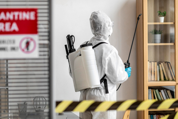 A person in a white protective suit sprays disinfectant in a room, ensuring a clean and safe environment.